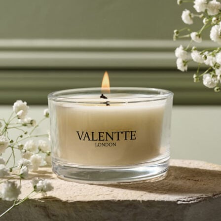 A close up of our 75 gram candle, lit with some flowers around